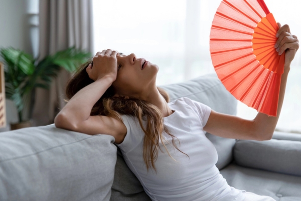 woman feeling hot indoors while using a hand fan due to hot spots at home
