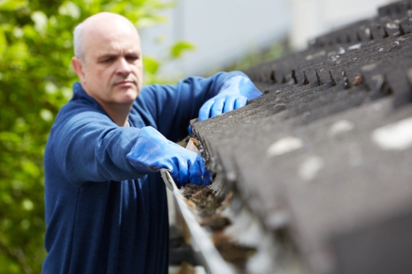 man clearing leaves from house gutter