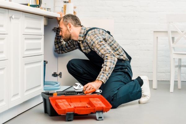 professional plumber holding a wrench and looking under the kitchen sink
