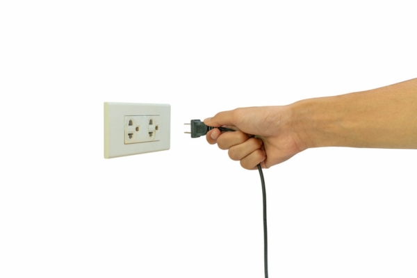 hand holding electrical plug about to plug at an outlet on the wall