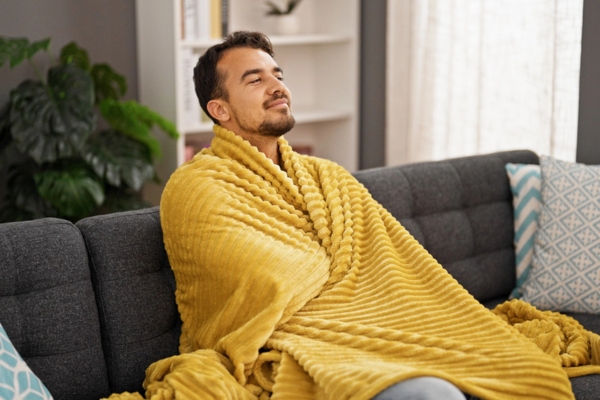 man wrapped in a blanket while sitting on a couch