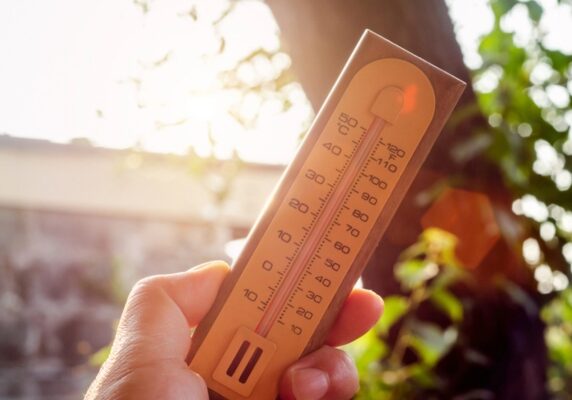 hand holding thermometer under the summer heat