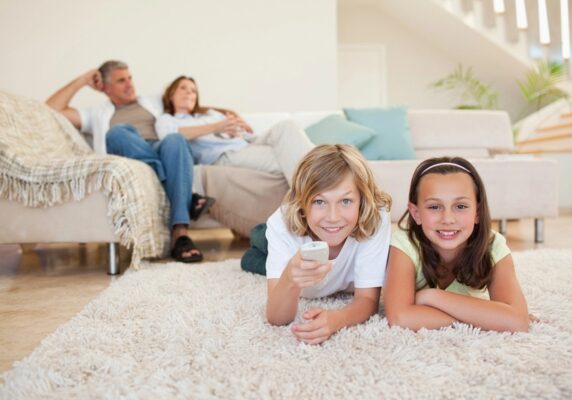 siblings lying on the carpet while watching TV and parents lounging on the couch depicting home comfort