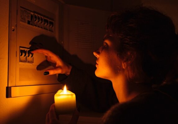 woman holding a candle examines electrical fuse box during power interruption